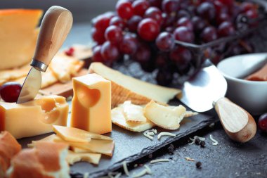 Üzüm, ekmek ve bal ile dekore edilmiş çeşitli peynir, siyah arduvaz kurulu