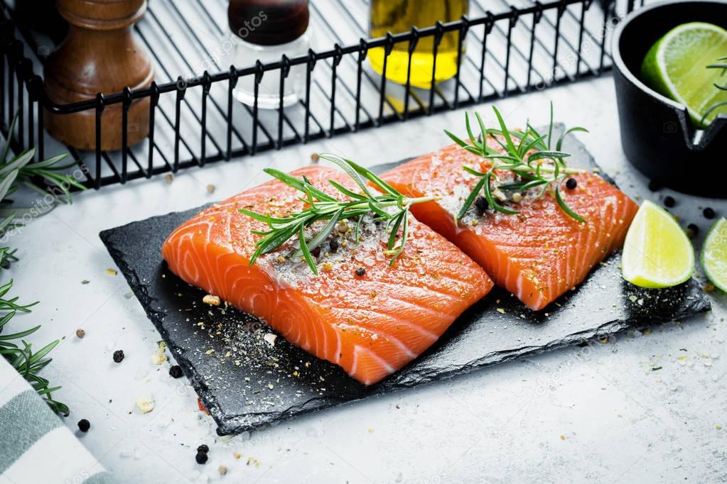 Two pieces of raw salmon fillet with fresh herb rosemary, spices and olive oil on black slate plate