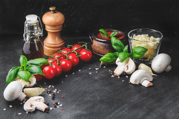 Ingredientes de pasta italiana. Tomates cereza, ajo, champiñones, albahaca, aceite de oliva, mozzarella y especias sobre fondo grunge oscuro con lugar para espacio de copia — Foto de Stock