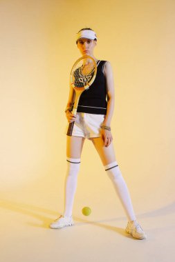  Spor kıyafetleri ve sarı arka planda beyaz spor ayakkabıları olan kız tenisçi.