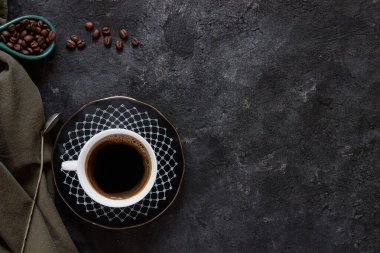 Koyu kahve fincanında beyaz kahve, koyu fonda kahve çekirdekleri yeşil bir bez ve antika bir kaşık.