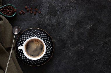 Koyu kahve fincanında beyaz kahve, koyu fonda kahve çekirdekleri yeşil bir bez ve antika bir kaşık.