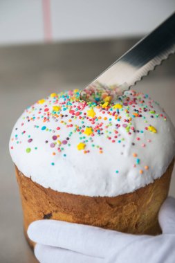 Beyaz eldivenli eller Paskalya pastasını beyaz süslemeli ve renkli süslemeli kes.