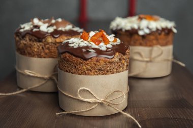 Çikolata, badem gevreği ve ahşap masada kurutulmuş kayısılarla süslenmiş kahverengi Paskalya pastaları. 