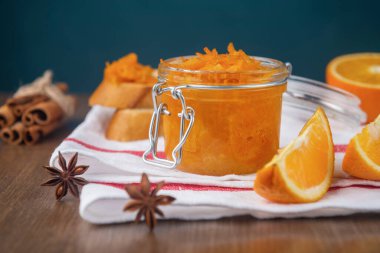 Bir kavanoz portakal reçeli beyaz bir peçeteye dilimlenmiş Fransız ekmeği, dilimlenmiş portakal, tarçın ve ahşap bir masada yıldız anason.