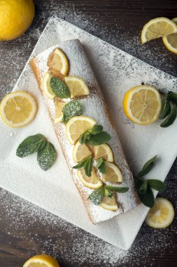 Limon dilimleri ve nane yapraklarıyla süslenmiş limonlu kek, beyaz tabakta tereyağlı kremalı limonlu pasta.