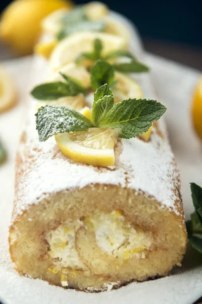 Lemon roll cake decorated with slices of lemon fruit and leaves of mint, lemon pie with butter cream on the white plate