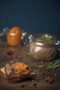 Kümes hayvanı ezmesi ve turuncu gam ile bir dilim ekmek, kümes hayvanları ezmeli cam kavanoz, badem ve biberiyeyle süslenmiş, ve ahşap bir masada turuncu reçelli kavanoz. Baharatla dekore edilmiş ev yapımı ciğer ezmesi.