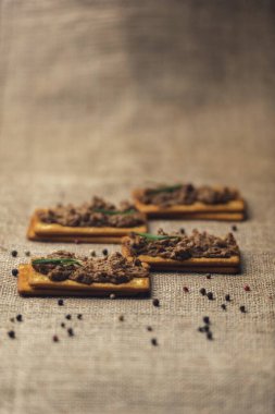 Çuval bezi ve ahşap zemin üzerinde kümes hayvanları ezmesi olan birkaç kraker, çuval ağacında baharatlarla süslenmiş ev yapımı karaciğer ezmesi.