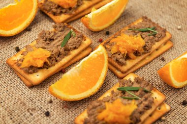 Kümes hayvanları ve portakal reçelli birkaç kraker, çuval bezinde bir dilim portakal meyvesi, çuval bezi masasında baharatlarla süslenmiş ev yapımı karaciğer ezmesi.