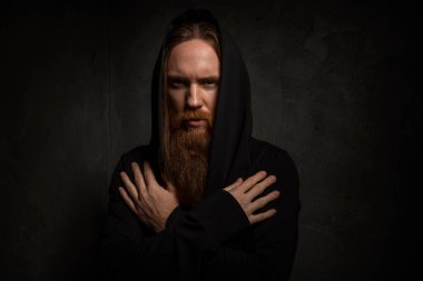 Siyah kapüşonlu, uzun saçlı ve sakallı adam.