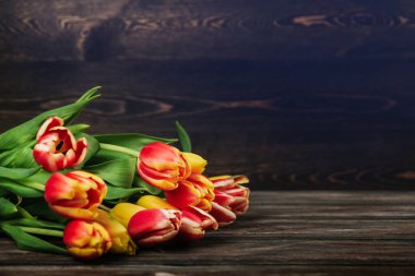 Kahverengi ahşap arka planda kırmızı, sarı ve pembe laleler.