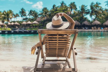 Genç bir bayan kumsalda bir şişe birayla plaj sandalyesinde oturup rahatlıyor.