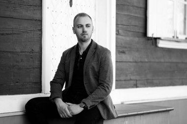 Sakallı genç adam binanın yanındaki merdivenlerde oturuyor ve yan tarafa bakıyor.