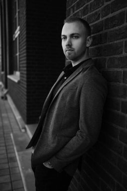 Ceketli, siyah duvarın yanında duran yakışıklı iş adamı siyah beyaz bir portre çiziyor.