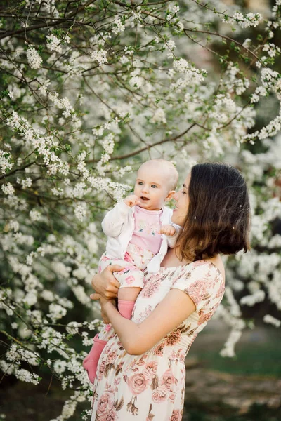 Anne, çiçek açan ağacın yanında küçük bir kız çocuğu tutuyor, bahar aile fotoğrafçılığı.