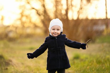 Gün batımında poz veren ve dal tutan güzel gülüşlü küçük bir kız.
