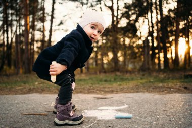 Gün batımında asfalta tebeşir parçası çizen küçük bir kız.
