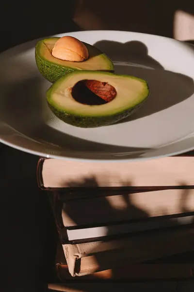 Beyaz cam tabaktaki avokado çok güzel ve bir yığın kitabın üzerinde.