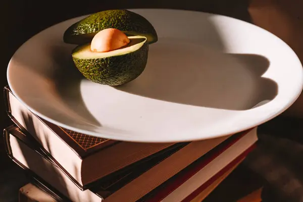 Beyaz cam tabaktaki avokado çok güzel ve bir yığın kitabın üzerinde.