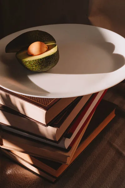 Beyaz cam tabaktaki avokado çok güzel ve bir yığın kitabın üzerinde.