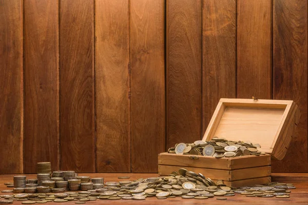 Masanın üzerinde bozuk para ve altın para yığınlarıyla dolu tahta bir kutu. Ahşap arka plan. Ekonomi, kazanç, kar ve para hakkındaki kavramsal imaj.