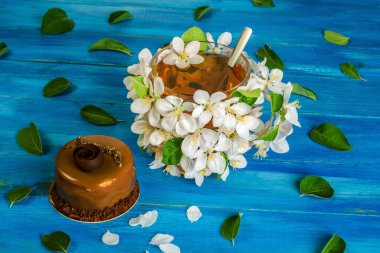 Elma çiçekleri ve güzel bir çikolatalı pastayla süslenmiş bir fincan çiçek çayı mavi bir ahşap masada yatıyor. Bahar içeceği kavramı. Yakın plan..