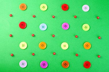 Yeşil bir yüzey üzerinde çok renkli düğmeler ve kırmızı boncuklar. Soyut desen.