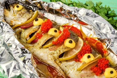 Limon, domates ve yeşillikle kaplanmış alabalık ızgarası, kırmızı havyar serpiştirilmiş. Mavi ahşap arka planda.