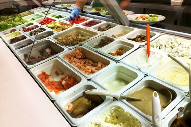 Büfede farklı salata tercihleri var. Farklı malzemeler - karides, domates, marul, balık, kızarmış ve ızgara sebze ve diğer çeşitli yiyecekler. Yakın plan..