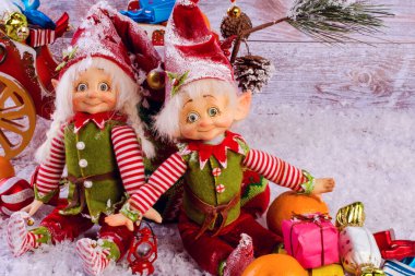 Komik noel elfleri, Noel çorabının yanında hafif ahşap arka planda otururlar. Mandalina ve hediyelerin yanında. Yakın plan..