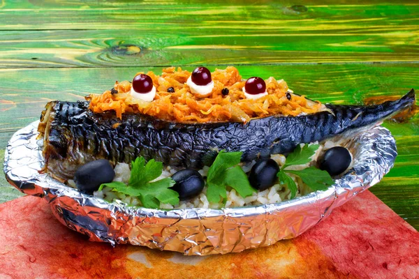 Havuç, zeytin ve maydanozla doldurulmuş fırınlanmış uskumru balığı folyoya sarılmış, içinde haşlanmış pirinç olan bir tabakta yatıyor. Yeşil ahşap arka planda. Yakın plan..