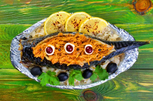 Havuç, zeytin ve maydanozla doldurulmuş fırınlanmış uskumru balığı folyoya sarılmış, içinde haşlanmış pirinç olan bir tabakta yatıyor. Yeşil ahşap arka planda. Üst düz manzara. Yakın plan..