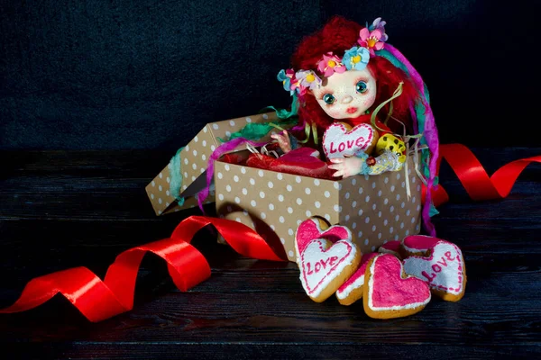 Oyuncak bebek bir hediye kutusunda kalbi ile oturuyor. Üzerinde 