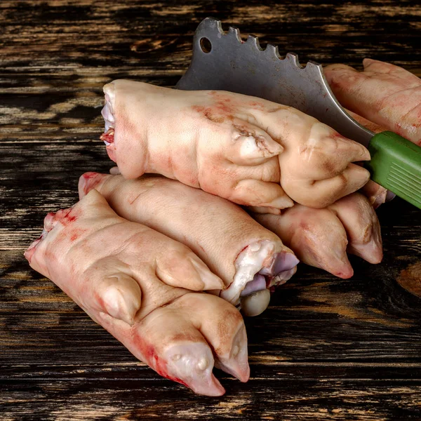Koyu ahşap tahtada çiğ domuz ayağı ya da bacakları. Yığınla var. Kesik bir baltayla. Et aşısı. Kare. Yakın plan..