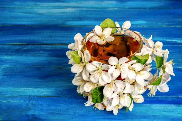 Elma çiçekleriyle süslenmiş bir fincan çiçek çayı mavi bir ahşap masada yatar. Bahar içeceği kavramı. Metin için cpace kopyala. Yakın plan..