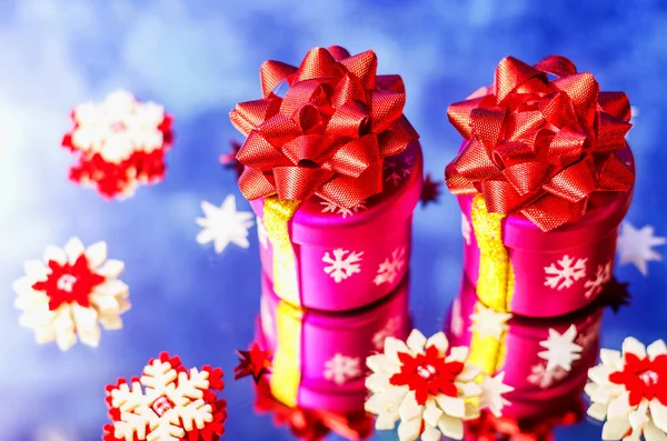 Ayna yüzeyinde iki pembe Noel hediyesi ve dekoratif kar taneleri. Yakın plan..