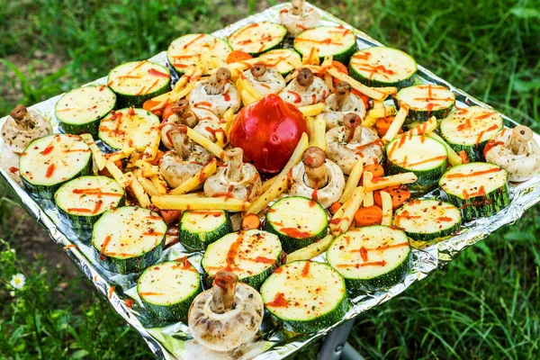 Pişirmeden önce folyoda çiğ sebze tepsisi. Tepsi metal bacaklı bir sandalyenin üzerinde. Yeşil çimenlerin arka planında.