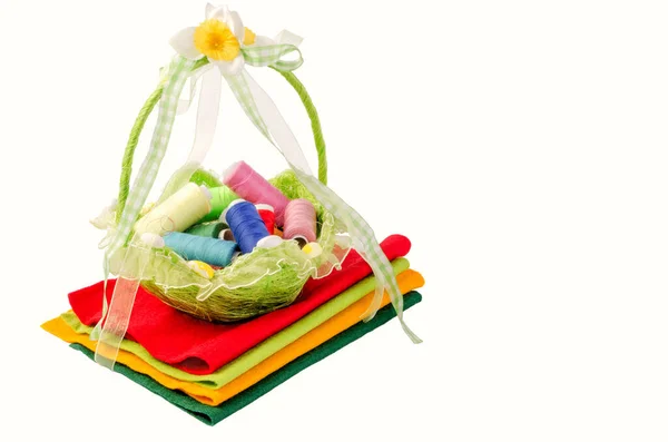 Çok renkli iplik makaralarının olduğu çok güzel bir hasır sepet çok renkli kumaş parçalarının üzerinde duruyor. Beyaz arka planda izole edilmiş. Yatay çekim.