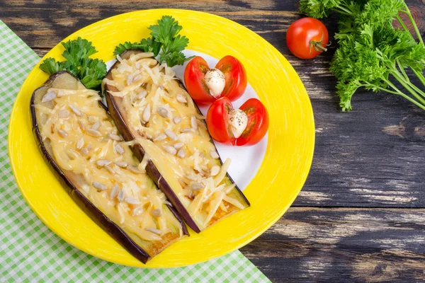 Parmesanlı fırında patlıcan, ayçekirdeği ve domates. Ahşap bir arka planda sarı bir çanakta. Maydanozun bir dalı yakında..