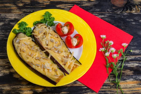 Parmesanlı fırında patlıcan, ayçekirdeği ve domates. Ahşap bir arka planda sarı bir çanakta. Kırmızı bir peçete ve tarla çiçeği yakında.. 