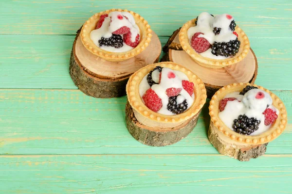 Süslü böğürtlenli ve kremalı tart. Mavi ahşap bir arka planda.