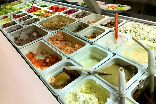 Büfede farklı salata tercihleri var. Farklı malzemeler - karides, domates, marul, balık, kızarmış ve ızgara sebze ve diğer çeşitli yiyecekler. Yakın plan..