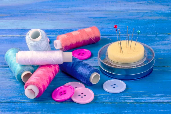 Sewing kit. Thread, pins and buttons. Handmade, sewing, needlework, hobby concept. On blue wooden  background.