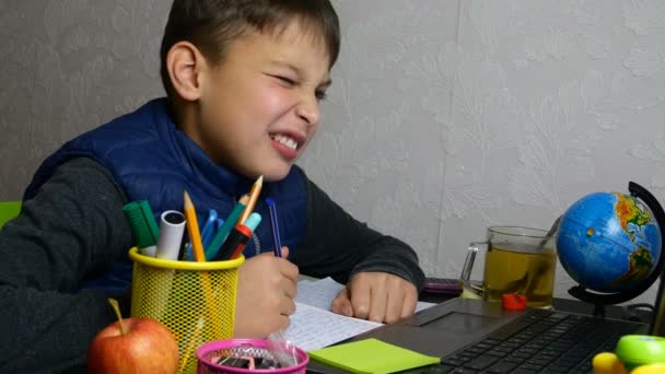 Distance learning. Funny schoolboy gets online education and does school homework during quarantine with notebook. He is grimacing and fooling around. Close-up portrait. — Stock Video