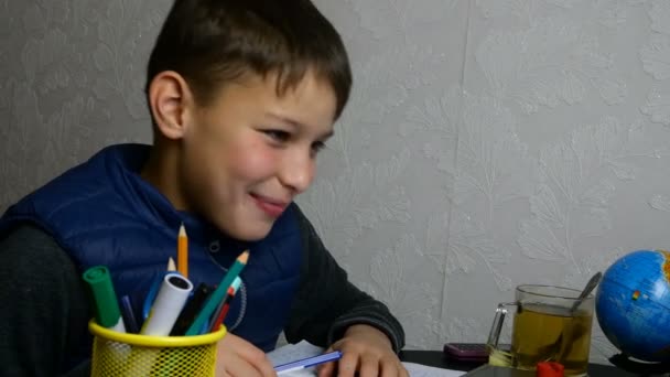 Distance learning. Funny schoolboy gets online education and does school homework during quarantine with notebook. He is grimacing and fooling around. Close-up portrait. — Stock Video