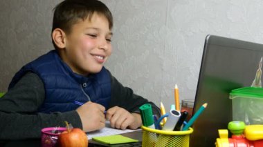 Uzaktan öğrenme, E-öğrenme. Yorgun okul çocuğu internetten eğitim alıyor ve karantina sırasında okul ödevi yapıyor. Masaüstünde okul malzemeleriyle oturuyor. Yakın plan portre.