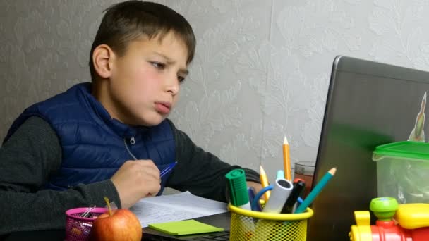 Aprendizaje a distancia, E-learning. Cansado, molesto, colegial obtiene educación en línea y hace la tarea escolar durante la cuarentena. Sentado en el escritorio con útiles escolares. Retrato de primer plano . — Vídeos de Stock