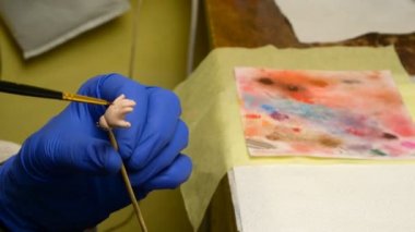 Oyuncak bebek yapmak. Usta kukla, ince fırçayla parmaklarını bebeklerin eline boyuyor. El yapımı oyuncak bebek yapma kavramı. Yakın plan. Kapalı.