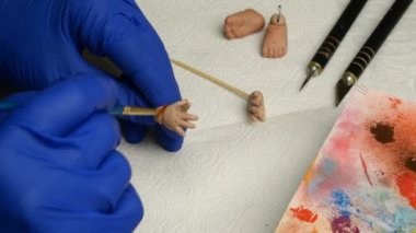 Oyuncak bebek yapmak. Usta kukla, ince fırçayla parmaklarını bebeklerin eline boyuyor. El yapımı oyuncak bebek yapma kavramı. Yakın plan..